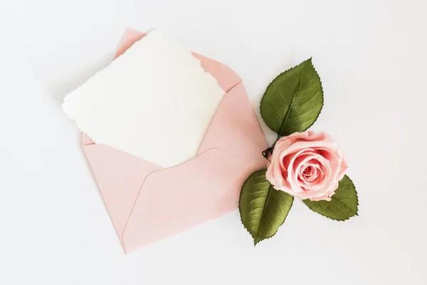 Roze envelop met witte kaart en rose. Plat leggen. — Stockfoto