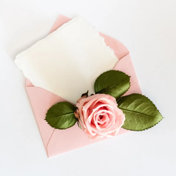 Roze envelop met witte kaart en rose. Plat leggen. — Stockfoto