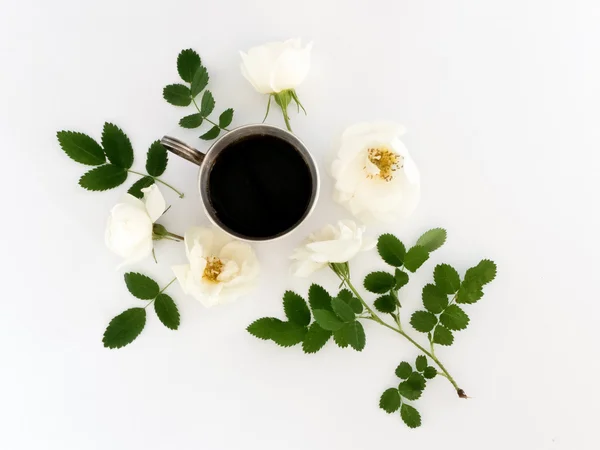 Tasse Kaffee mit Blüten und grünen Blättern auf weißem Hintergrund. flache Lage, Draufsicht — Stockfoto