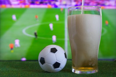 Bardak bira ve tv, futbol maçı arka planda