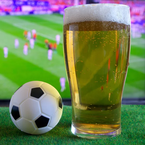 Glass of beer and tv, football match in background — Stock Photo, Image