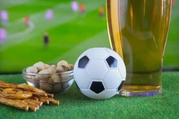 Glass of beer and tv, football match in background — Stock Photo, Image