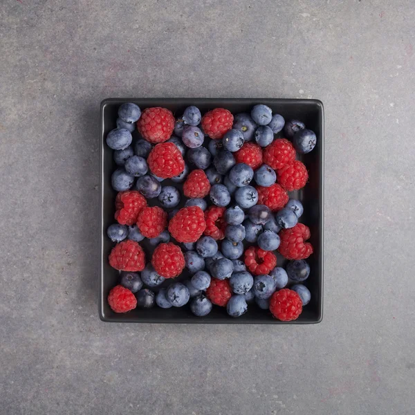 Blueberries and raspberries in a bowl on rusty grey background. Top view — Stock Photo, Image