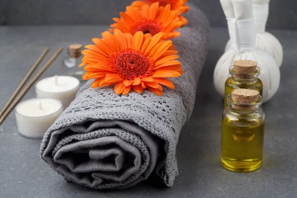 SPA ainda vida com toalhas, óleo, bolas de massagem e flores de gerbera em uma superfície cinza — Fotografia de Stock