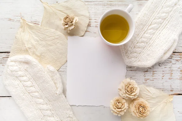 Beyaz ahşap arka plan üzerinde eldiven, çiçek ve boş kart ile çay Fincan — Stok fotoğraf