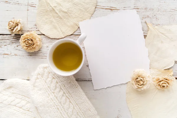 Xícara de chá com luvas, flores e cartão em branco sobre fundo de madeira branca — Fotografia de Stock
