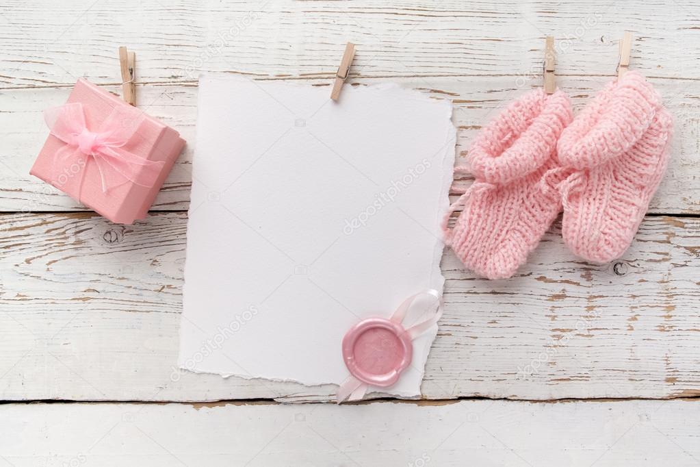 pink babys booties. Small girls sock, blank card with wax seal and present box on white wooden background