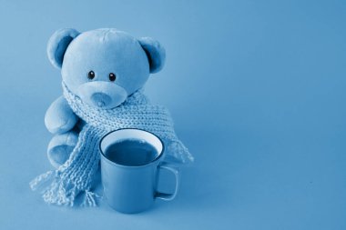 Mavi arka planda eşarp ve bir fincan kahve olan mavi bir oyuncak ayı. Mavi Pazartesi konsepti.