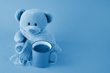 Blue teddy bear with scarf and cup of coffee on blue background. Blue monday concept. clipart