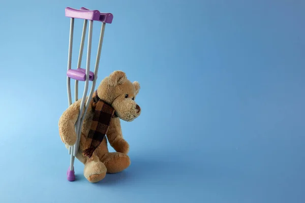 Ziua internaţională a persoanelor cu dizabilităţi. Ursuleț de pluș cu cârje pe fundal albastru . — Fotografie, imagine de stoc