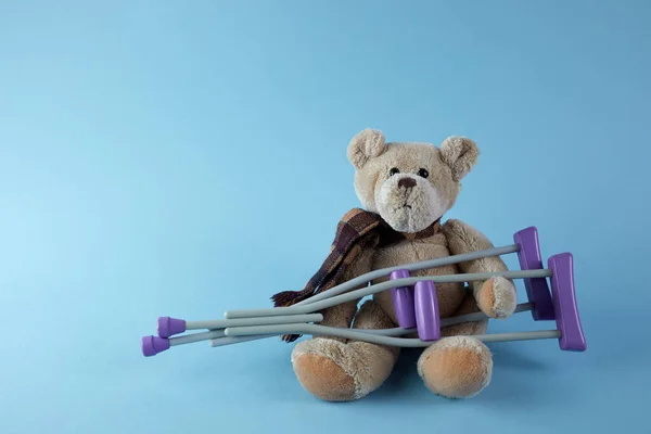 Internationaler Tag der Menschen mit Behinderungen. Teddybär mit Krücken auf blauem Hintergrund. — Stockfoto