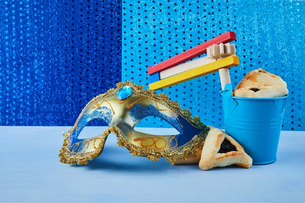 Concepto de celebración Purim con galletas hamantashen, máscara Purim y ruidoso juguete sobre fondo azul — Foto de Stock