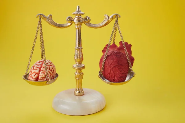 Cérebro e coração em balança de equilíbrio no fundo amarelo — Fotografia de Stock