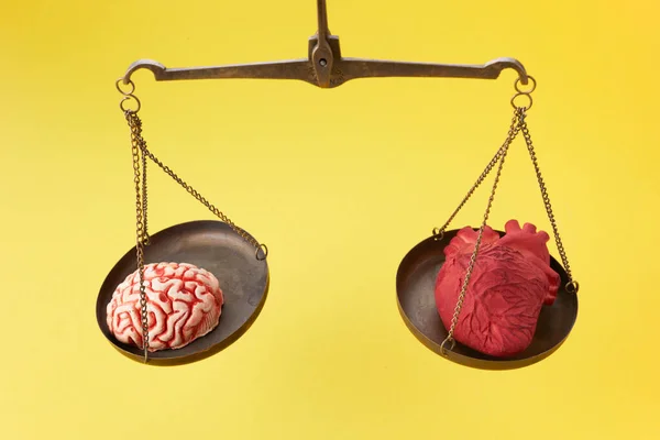 Cérebro e coração em balança de equilíbrio no fundo amarelo — Fotografia de Stock