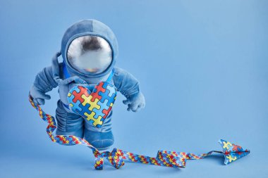Otizm farkındalığı. Mavi pelüş astronot oyuncağı, bulmaca kalpli, otizm sembollü, mavi arka planda