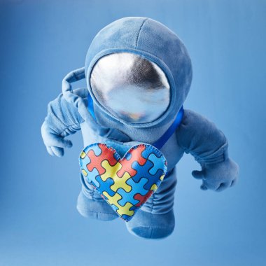 Dünya Otizmi farkındalık günü geçmişi. Mavi pelüş astronot oyuncağı, bulmaca kalpli, otizm sembollü, mavi arka planda