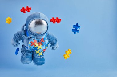 Dünya Otizmi farkındalık günü geçmişi. Mavi pelüş astronot oyuncağı, bulmaca kalpli, otizm sembollü, mavi arka planda