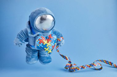 Dünya Otizmi farkındalık günü geçmişi. Mavi pelüş astronot oyuncağı, bulmaca kalpli, otizm sembollü, mavi arka planda