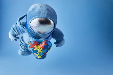 Dünya Otizmi farkındalık günü geçmişi. Mavi pelüş astronot oyuncağı, bulmaca kalpli, otizm sembollü, mavi arka planda