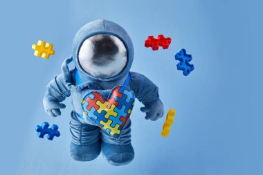 Dünya Otizmi farkındalık günü geçmişi. Mavi pelüş astronot oyuncağı, bulmaca kalpli, otizm sembollü, mavi arka planda