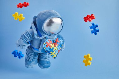 Dünya Otizmi farkındalık günü geçmişi. Mavi pelüş astronot oyuncağı, bulmaca kalpli, otizm sembollü, mavi arka planda