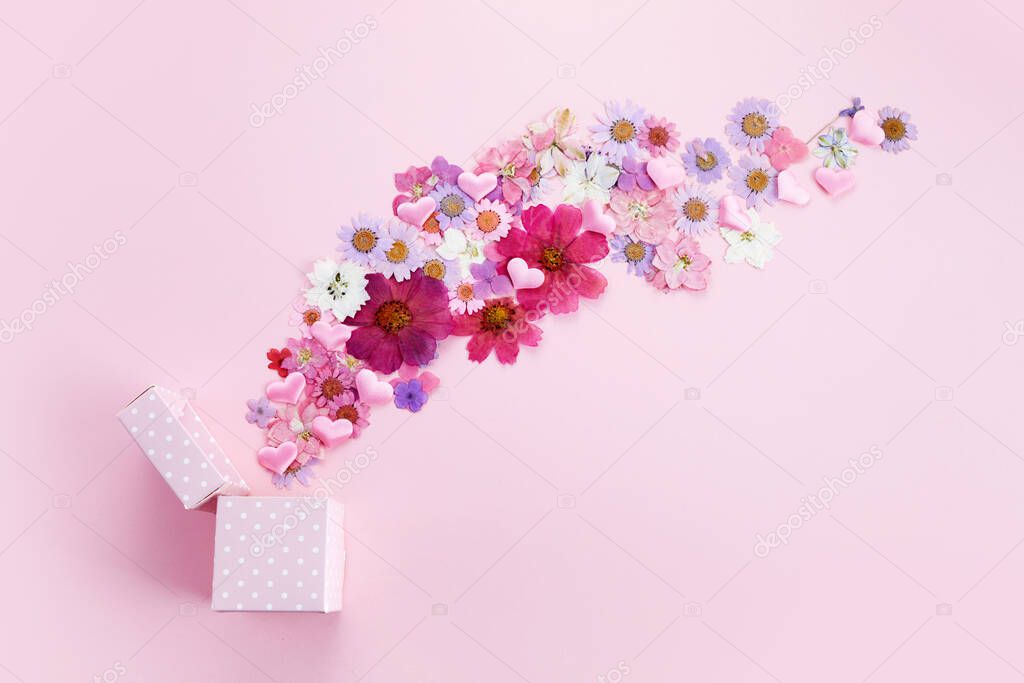 Gift box with flying coloful flowers on pink background. Flat lay. Top view