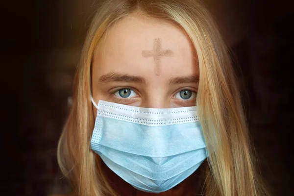 Meisje met kruis van as op voorhoofd met gezichtsmasker. Aswoensdag concept. — Stockfoto