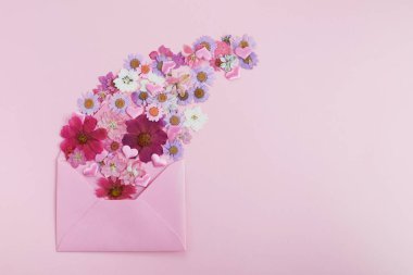 Pembe arka planda yabani renkli çiçeklerle kaplı bir zarf. Aşk konsepti. Düz yatıyordu.