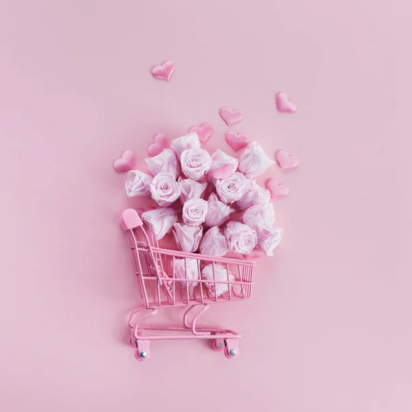 Carrito de compras con rosas rosadas y corazones sobre fondo rosa. Concepto románico — Foto de Stock