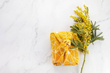 Pamuklu kumaşın sarı mimoza çiçekli Furoshiki eko tarzında paketlenmiş halinin üst görüntüsü. Kadın ya da Anneler Günü kutlamaları.