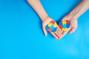 Father and autistic son hands holding jigsaw puzzle heart shape. Autism spectrum disorder family support concept. World Autism Awareness Day clipart