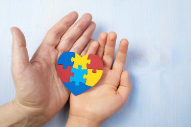 Father and autistic son hands holding jigsaw puzzle heart shape. Autism spectrum disorder family support concept. World Autism Awareness Day clipart