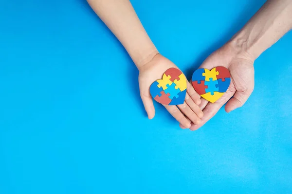 Father and autistic son hands holding jigsaw puzzle heart shape. Autism spectrum disorder family support concept. World Autism Awareness Day