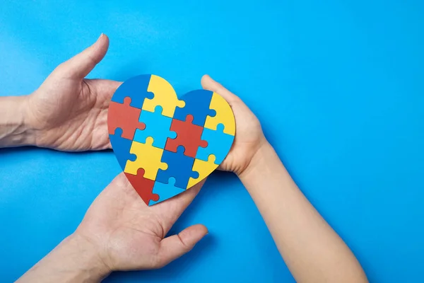 Padre e figlio autistico mani che tengono puzzle a forma di cuore. Autismo spettro disordine famiglia concetto di sostegno. Giornata mondiale della consapevolezza dell'autismo — Foto Stock