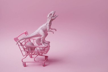 Alışveriş arabası ve pembe arka planda yumurtaları olan bir dinozor. Paskalya mega satış konsepti.