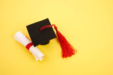 Sarı arka planda diplomalı akademik şapka. Mezuniyet teması