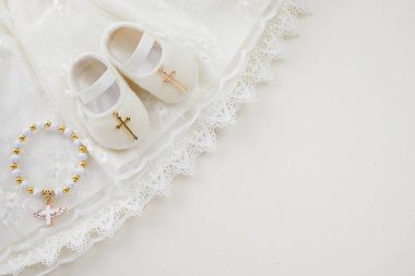Vaftiz arkaplanı, bebek elbisesi, ayakkabısı ve haçı pastel arka planda.