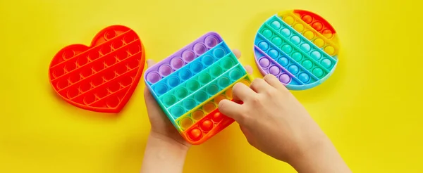 Kid hands playing with colorful pop It fidget toy. Colorful antistress sensory toy fidget push pop it.