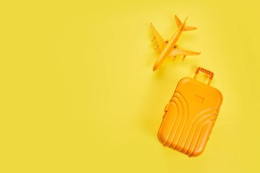 Sarı zemin üzerinde uçak olan düz sarı bir bavul. Seyahat kavramı