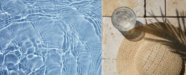 Summer vacation. Hat on the travertine stone by the beautiful swimming pool. Blue sea surface with waves, texture water. — Stock Photo, Image