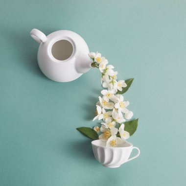 Yeşil arka planda yasemin çiçekli çaydanlık ve çay fincanı düzeni. Yasemin çayı..