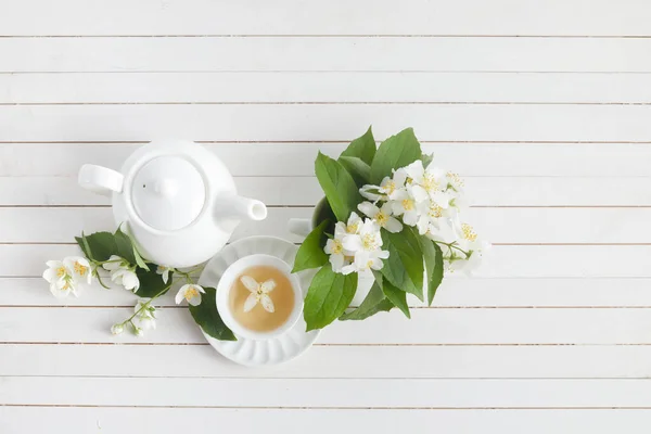 Jasmine flowers and teapot on white wooden background. Herbal tea of jasmine flower. Flat lay.