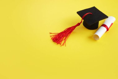 Sarı arka planda diplomalı akademik şapka. Mezuniyet teması
