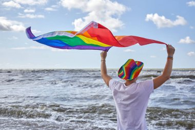 Deniz kenarında duran ve LGBTQ gurur bayrağını tutan adam. LGBTQ kavramı