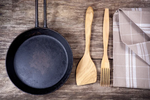 Frying pan and kitchen utensils on wooden table — Stock Photo, Image