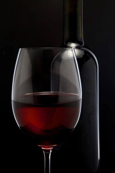 Copo de vinho tinto e uma garrafa em fundo preto — Fotografia de Stock