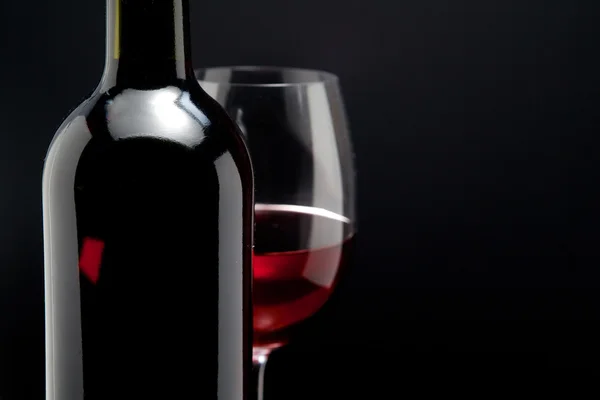 Copa de vino tinto y una botella en fondo negro — Foto de Stock