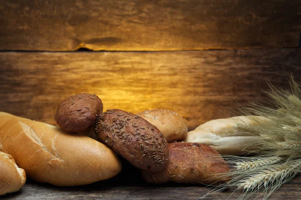 Pão fresco e trigo na madeira — Fotografia de Stock