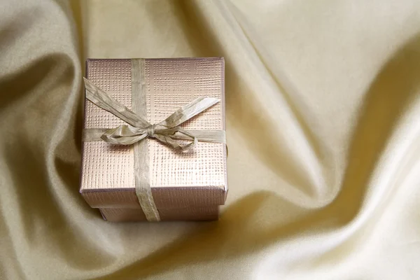 Golden box with ribbon on golden silk — Stock Photo, Image