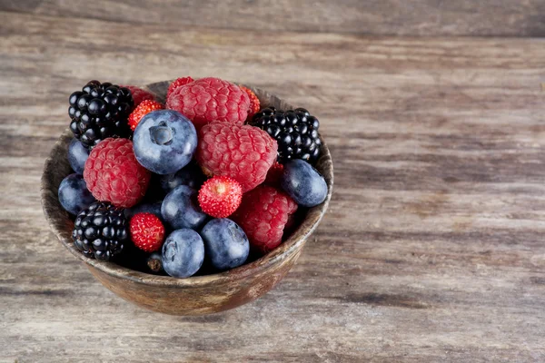 Assorted berries in bowl on wood — Stock Photo, Image